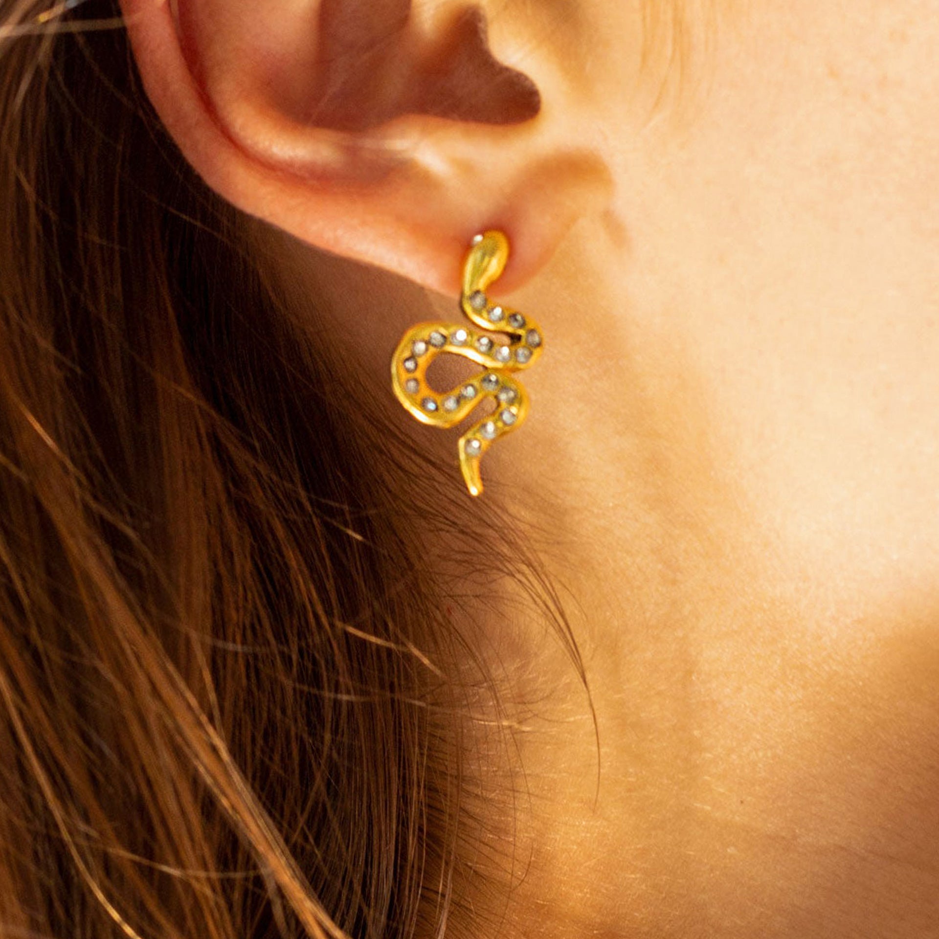 Gold snake earrings with rhinestones worn by female model in natural light