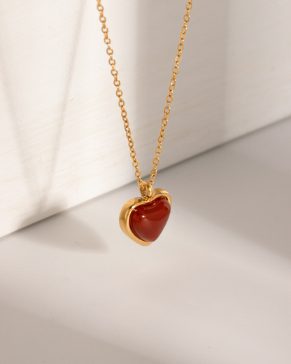 Gold necklace with a heart-shaped red stone pendant on a light background
