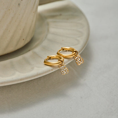 Close-up of gold teddy bear hoop earrings on ceramic plate, minimal chic style