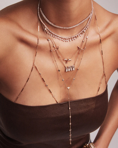 Close-up of a person wearing multiple necklaces with a neutral background