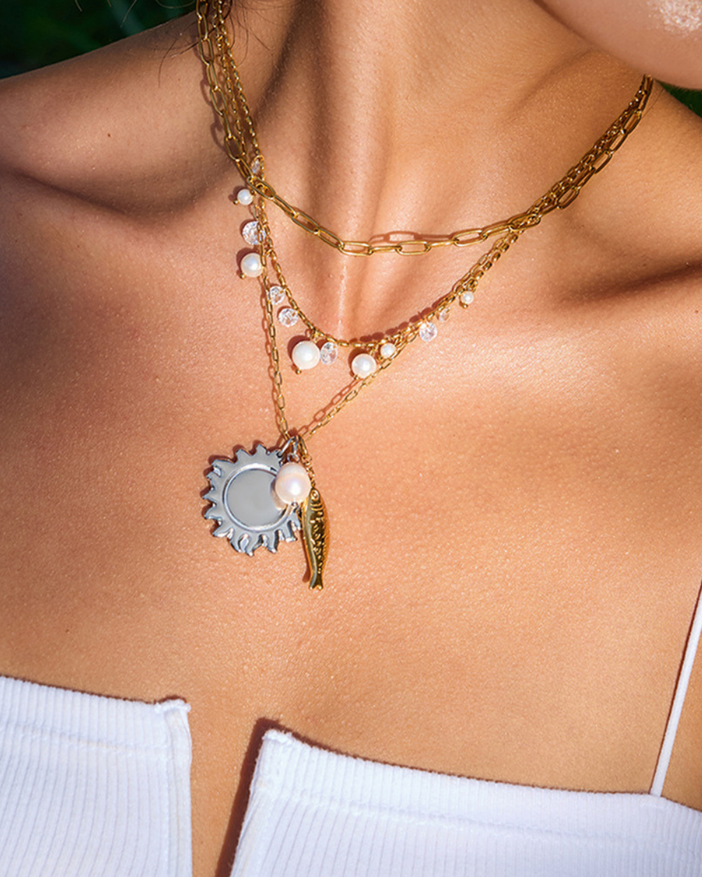 Close-up of a person wearing multiple necklaces with a gear charm and pearl pendant.
