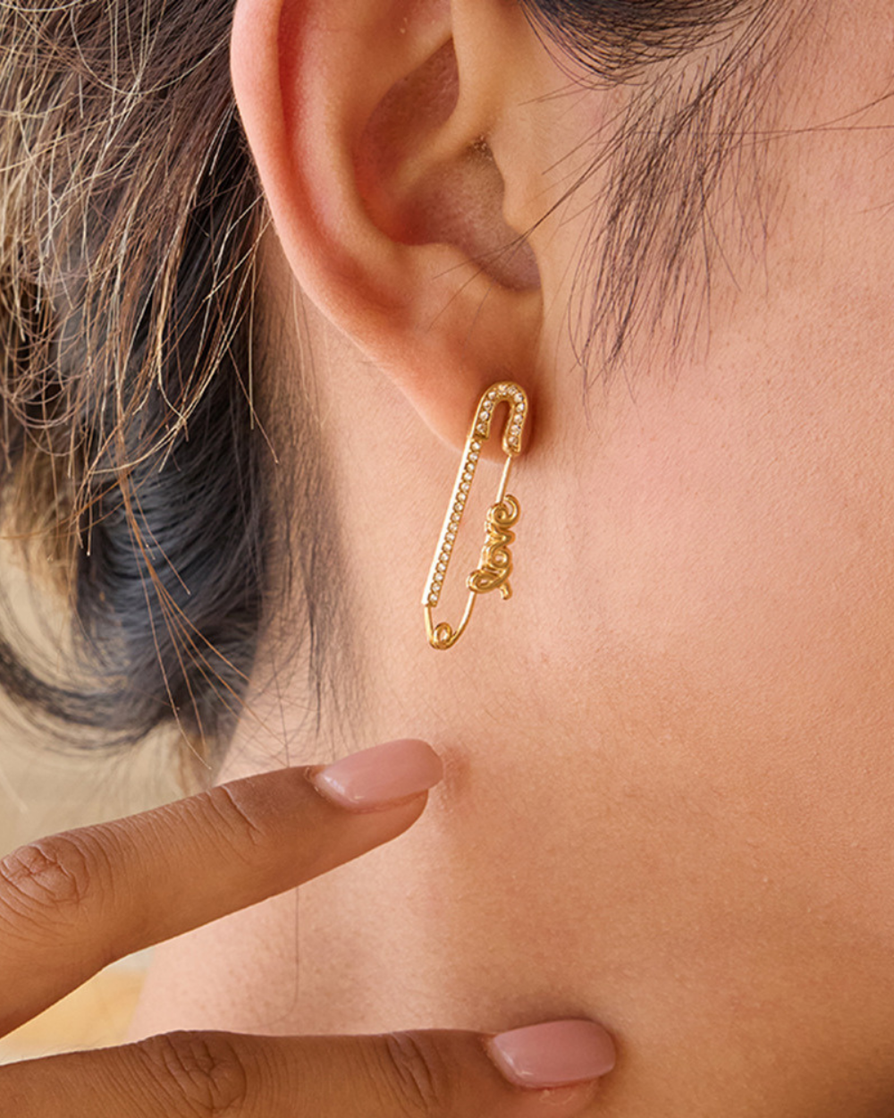 A woman's ear wearing a gold "Love" safety pin earring, showcasing its size and fit.