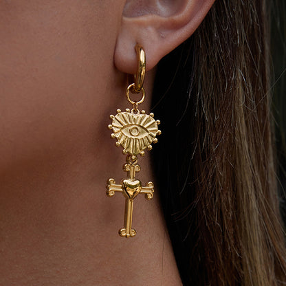 Gold earring with sunburst design and cross detail worn by a person.