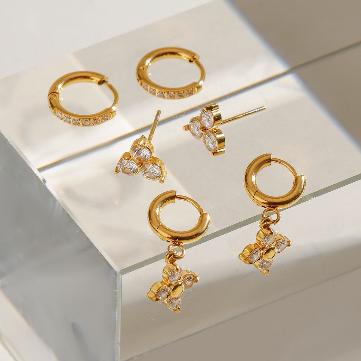 Gold hoop earrings with floral-shaped CZ drop charms, shown in daylight