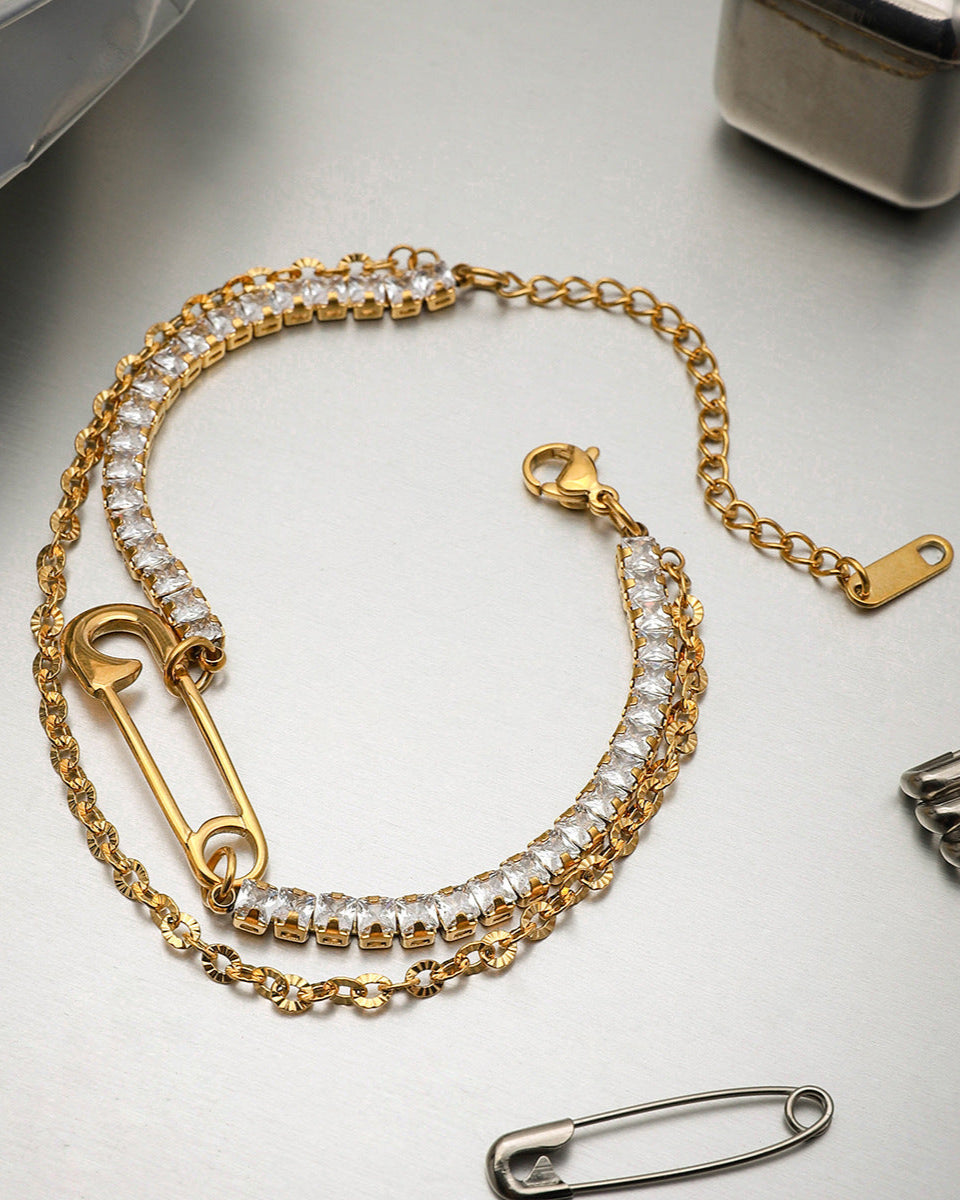 Top view of elegant gold bracelet with square-cut rhinestones and a unique safety pin charm