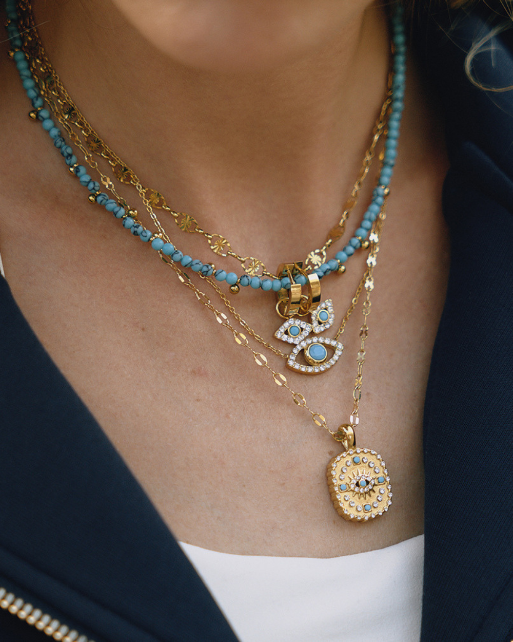 Model wearing gold Evil Eye necklace with blue stone pendant layered with other chains, stylish casual look.