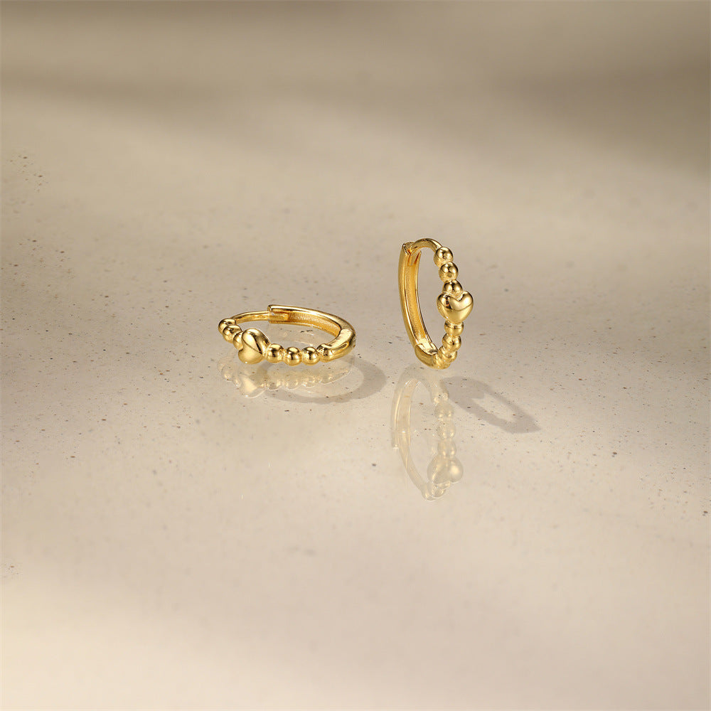 Pair of gold huggie hoops with mini heart detail on white background