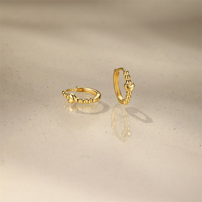 Pair of gold huggie hoops with mini heart detail on white background