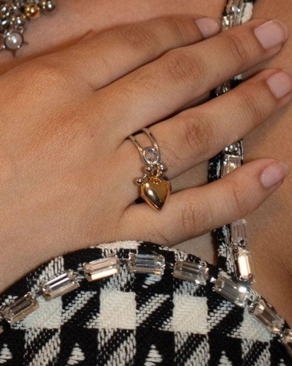 Close-up of a hand wearing a gold ring with a heart design on a patterned fabric background.