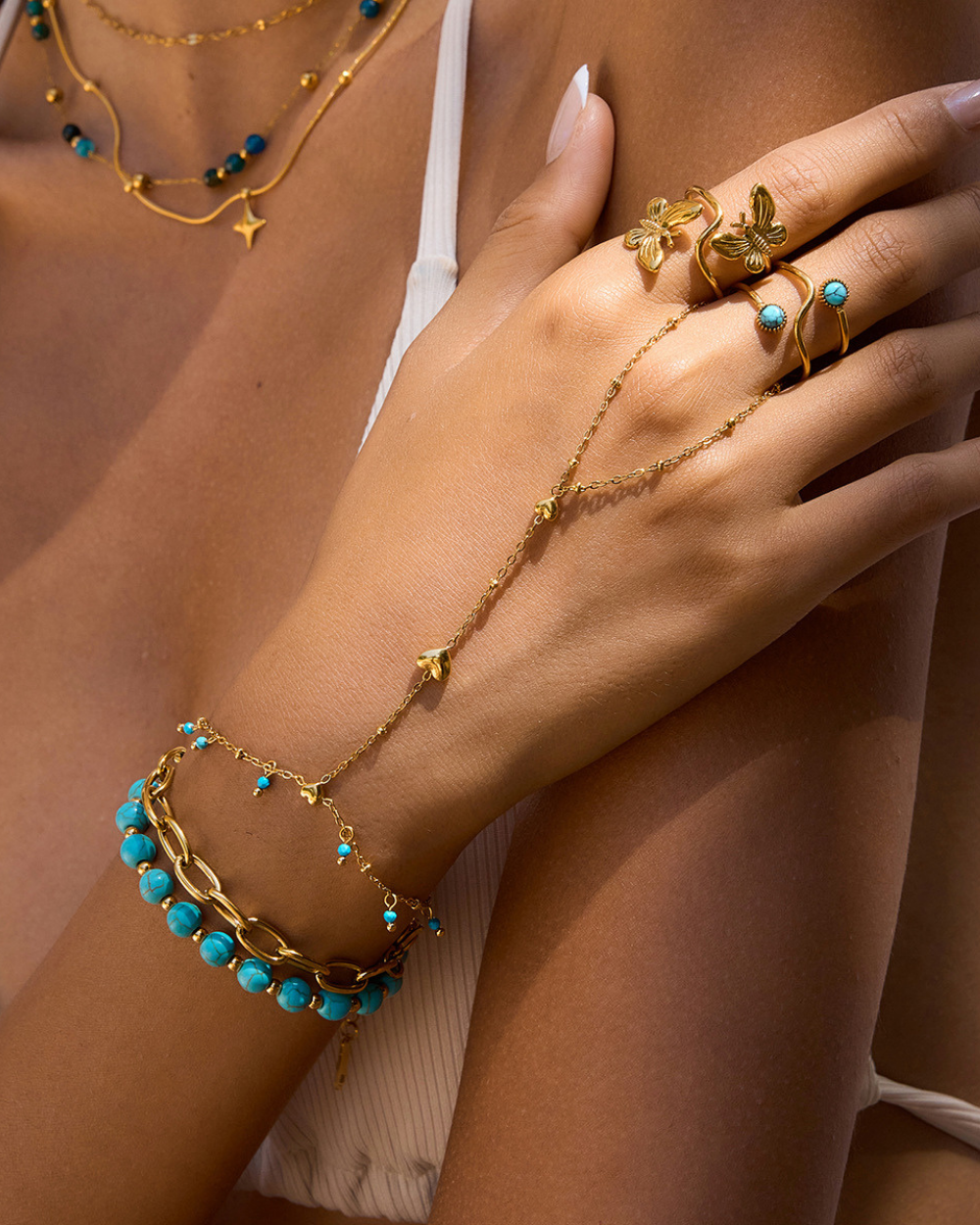 Close-up of a hand wearing gold jewelry with turquoise stones on a neutral background
