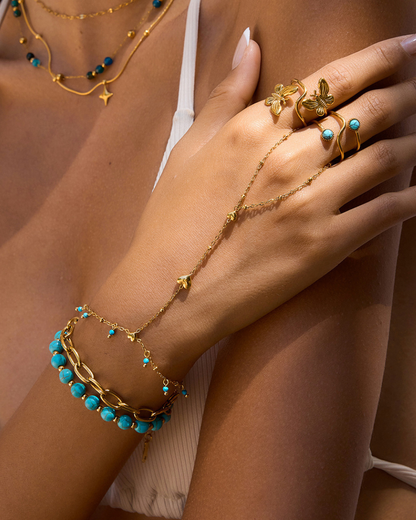 Close-up of a hand wearing gold jewelry with turquoise stones on a neutral background