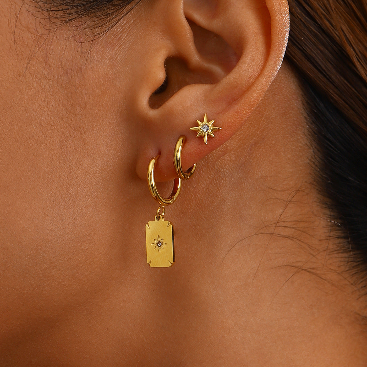 Close-up of model wearing starburst studs and rectangle tag earrings in gold finish