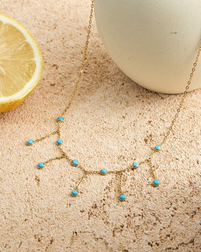 Gold necklace with turquoise stones on a textured surface next to a lemon and a white ball.