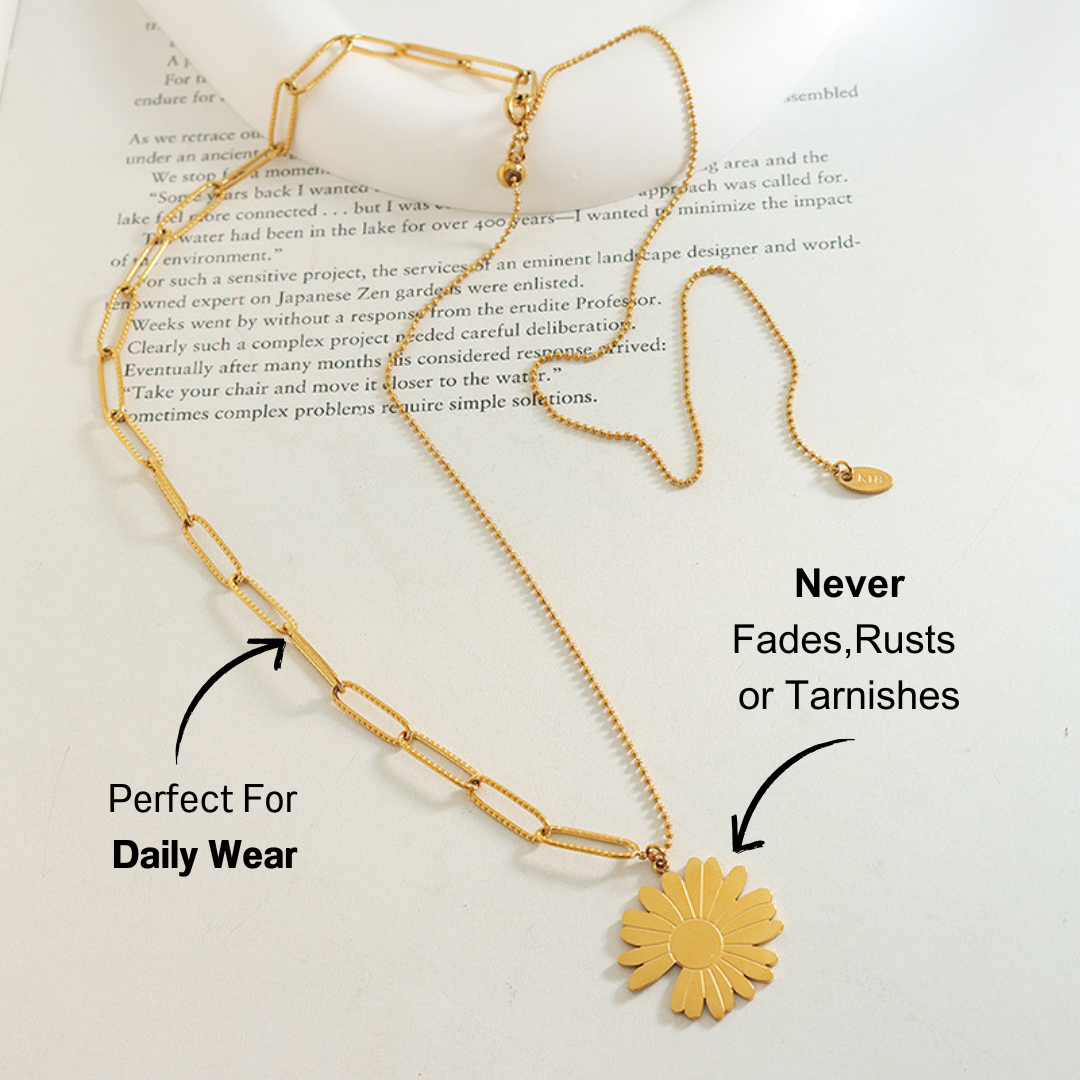 lose-up of daisy pendant necklace on flat lay, paired with dried flowers and an open book, emphasizing a subtle, stylish vibe.