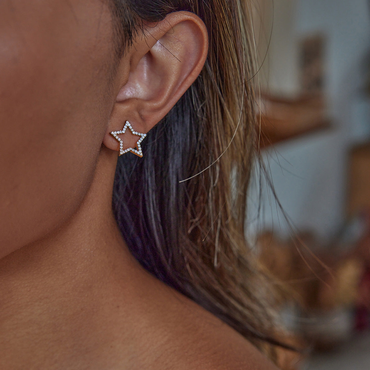 Model wear shimmering star-shaped earrings next to circular rhinestone pieces