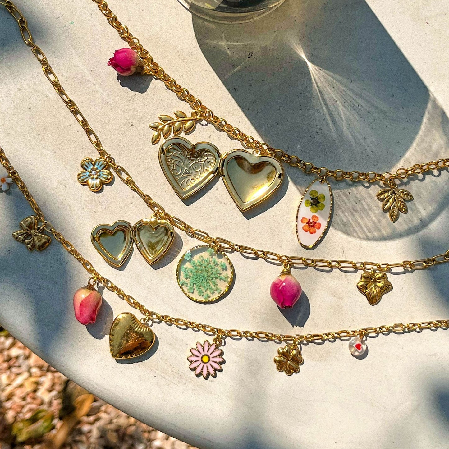 Bohemian gold necklace featuring dried flower resin charm, heart pendant and rosebud charm on white table