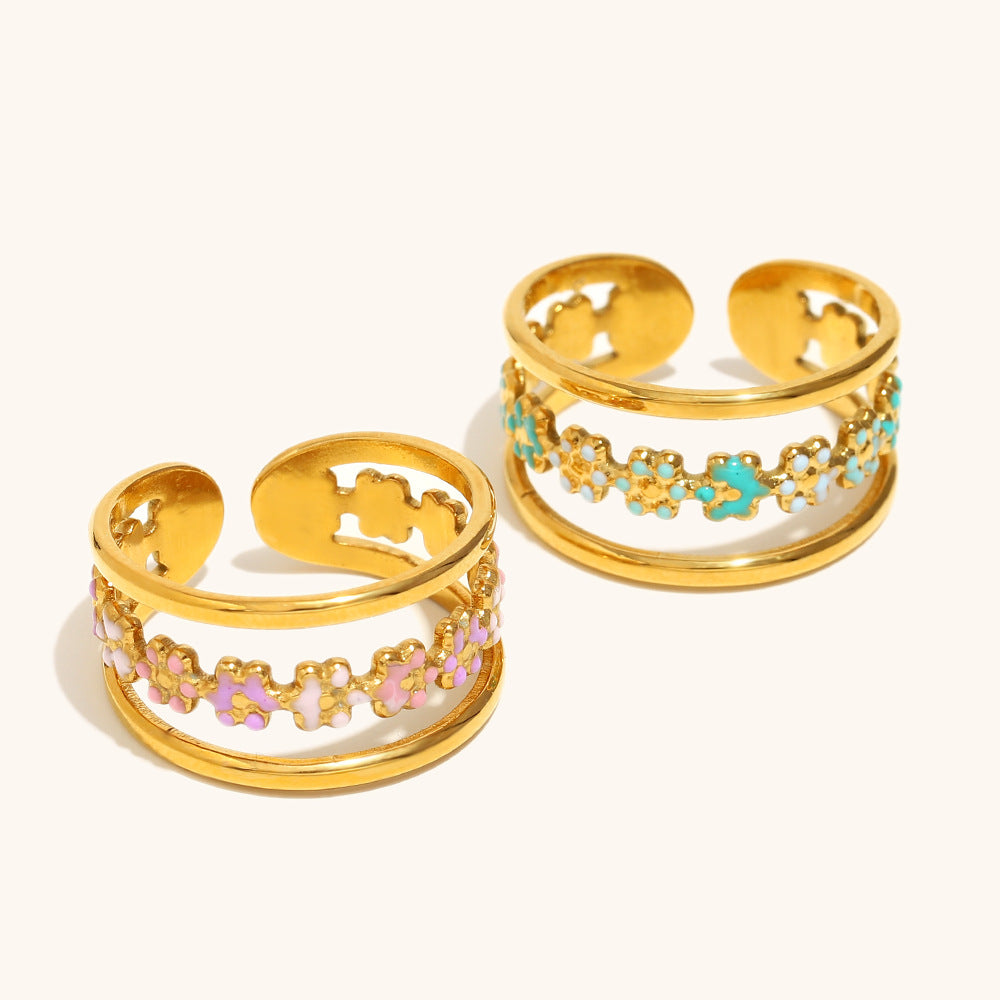 Set of two gold enamel rings in green and pink floral design, beach-inspired display.