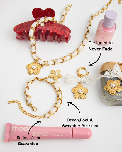 Gold chain with floral pendants, red hair clips, pink lip balm, and bottle on a white background.