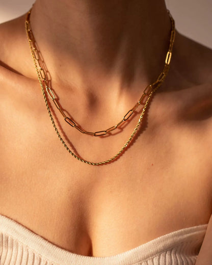 Close-up of a person wearing a gold chain necklace with a neutral background