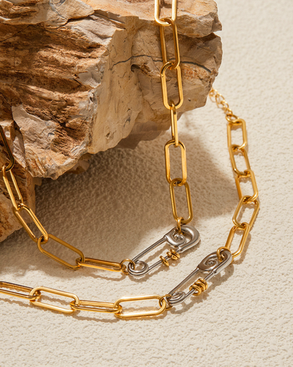 Gold chain necklace with a silver clasp on a textured beige surface