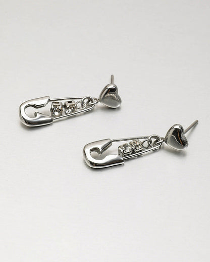 Studio shot of silver heart-shaped earrings with hanging safety pin and rhinestones.