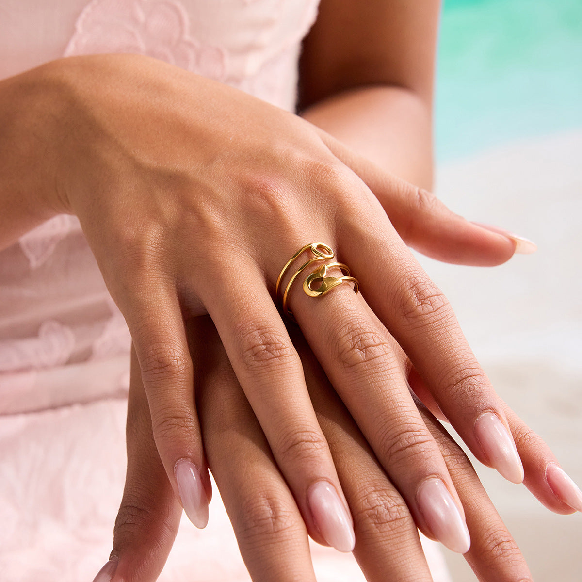 Close-up of model wearing bold gold safety pin ring by the poolside