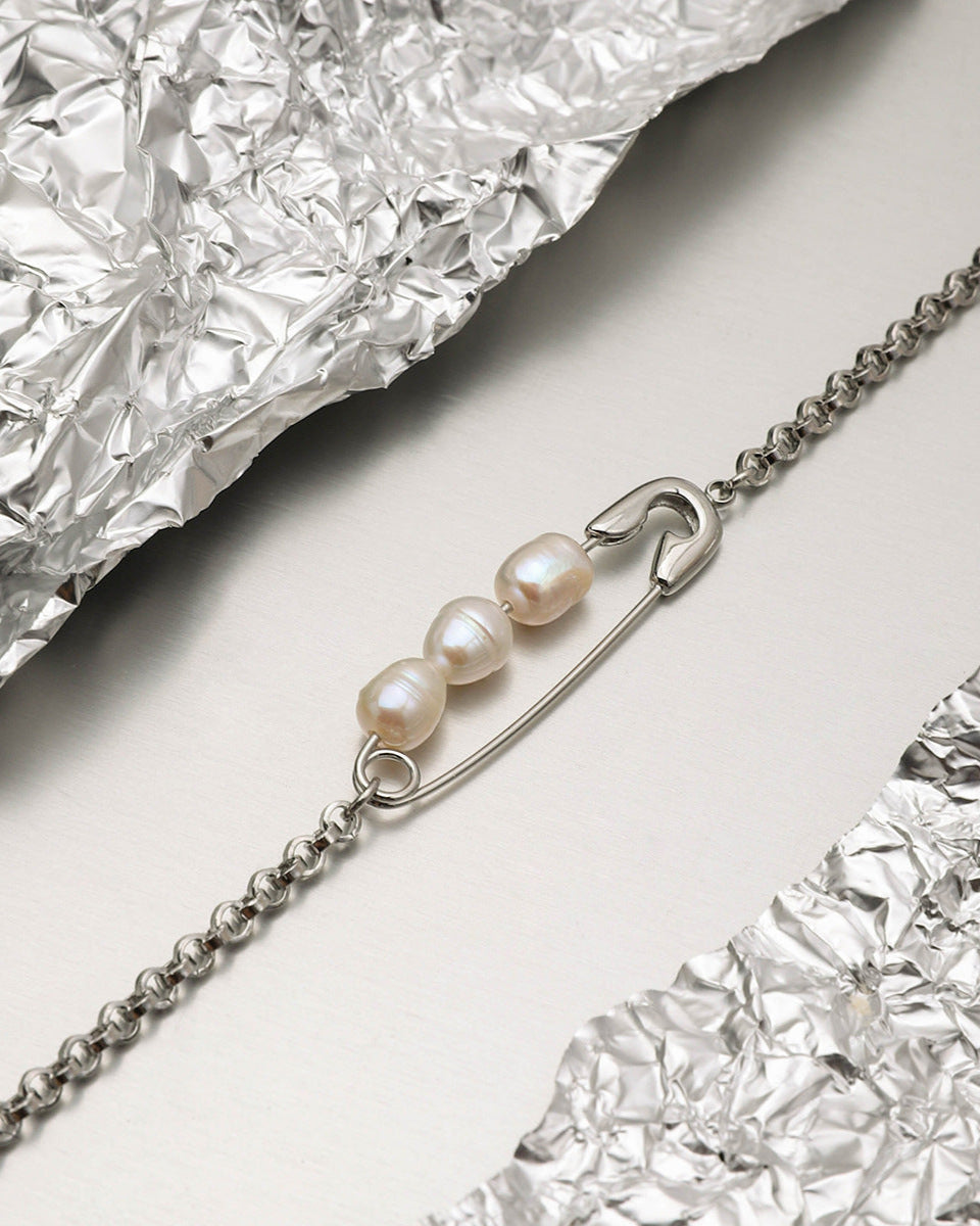 Close-up of safety pin necklace featuring three real pearls, placed on crinkled foil background