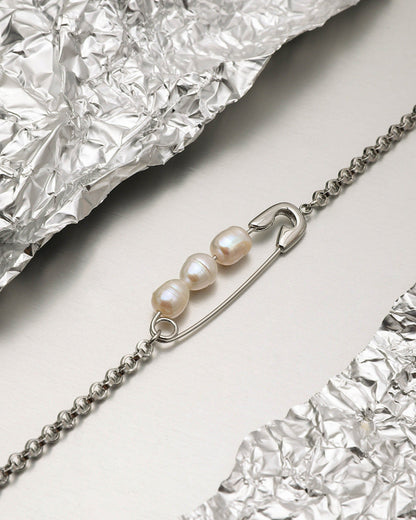 Close-up of safety pin necklace featuring three real pearls, placed on crinkled foil background