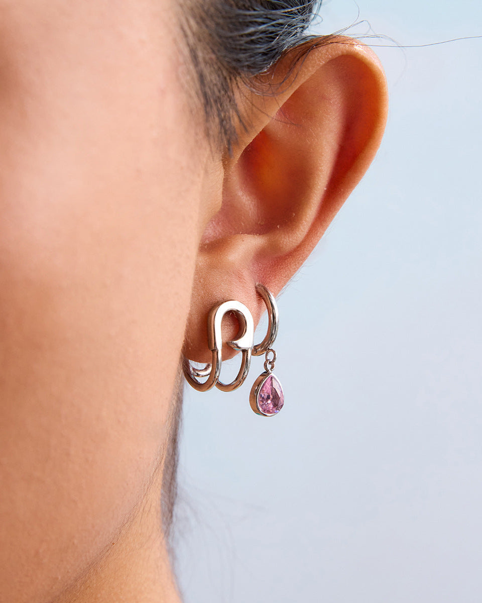 Model wears two earrings, one bold double hoop, the other with pink teardrop charm, urban punk style