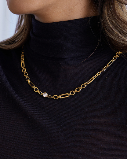 Gold chain necklace with a pearl pendant worn by a person in a black turtleneck.
