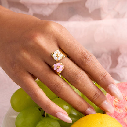 Gold ring with dual flower accents worn on female hand, styled with pastel dress