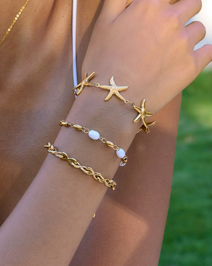 Gold starfish and chain bracelet on a wrist with a blurred green background