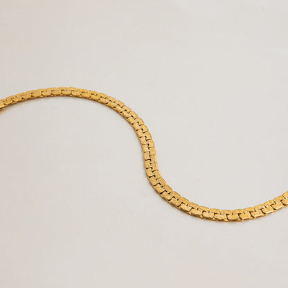 Wavy gold bracelet chain captured in a soft curve on marble surface