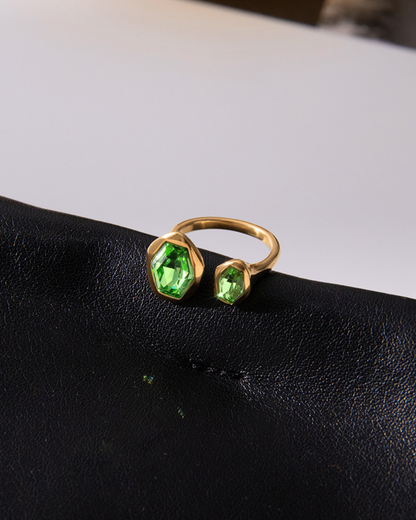 Gold ring with green gemstones on a black surface
