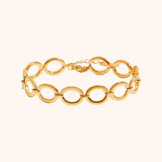 Close-up of polished gold ellipse link bracelet on cream background, highlighting smooth finishes