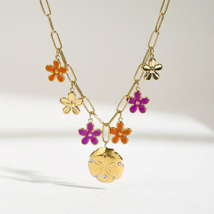Bright lighting shows purple and orange flower pendants with a gold sand dollar charm on a statement chain.