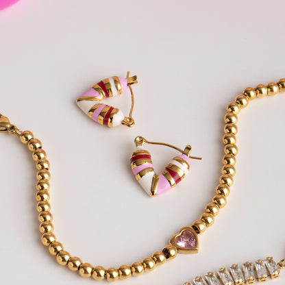 Close-up of heart-shaped hoop earrings in pink and white with gold details on white background