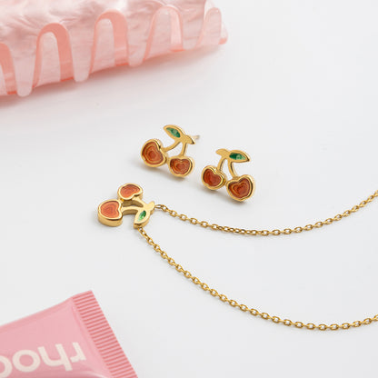 Cherry-themed gold earrings and necklace on a white background with pink tissue paper.