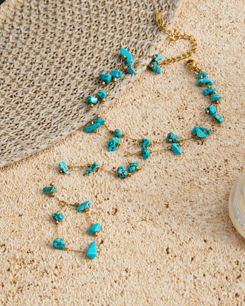 Turquoise necklace with gold chain on a textured beige surface