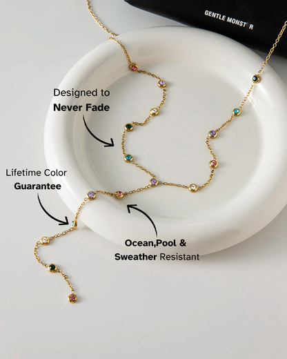 Gold necklace with colored beads on a white dish, featuring text about its features.