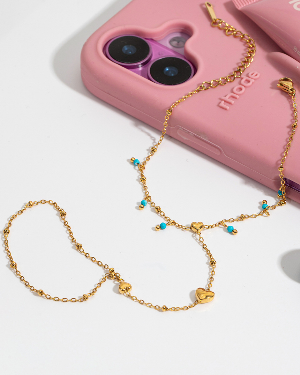 Gold chain with heart and turquoise bead details in front of a pink phone case.
