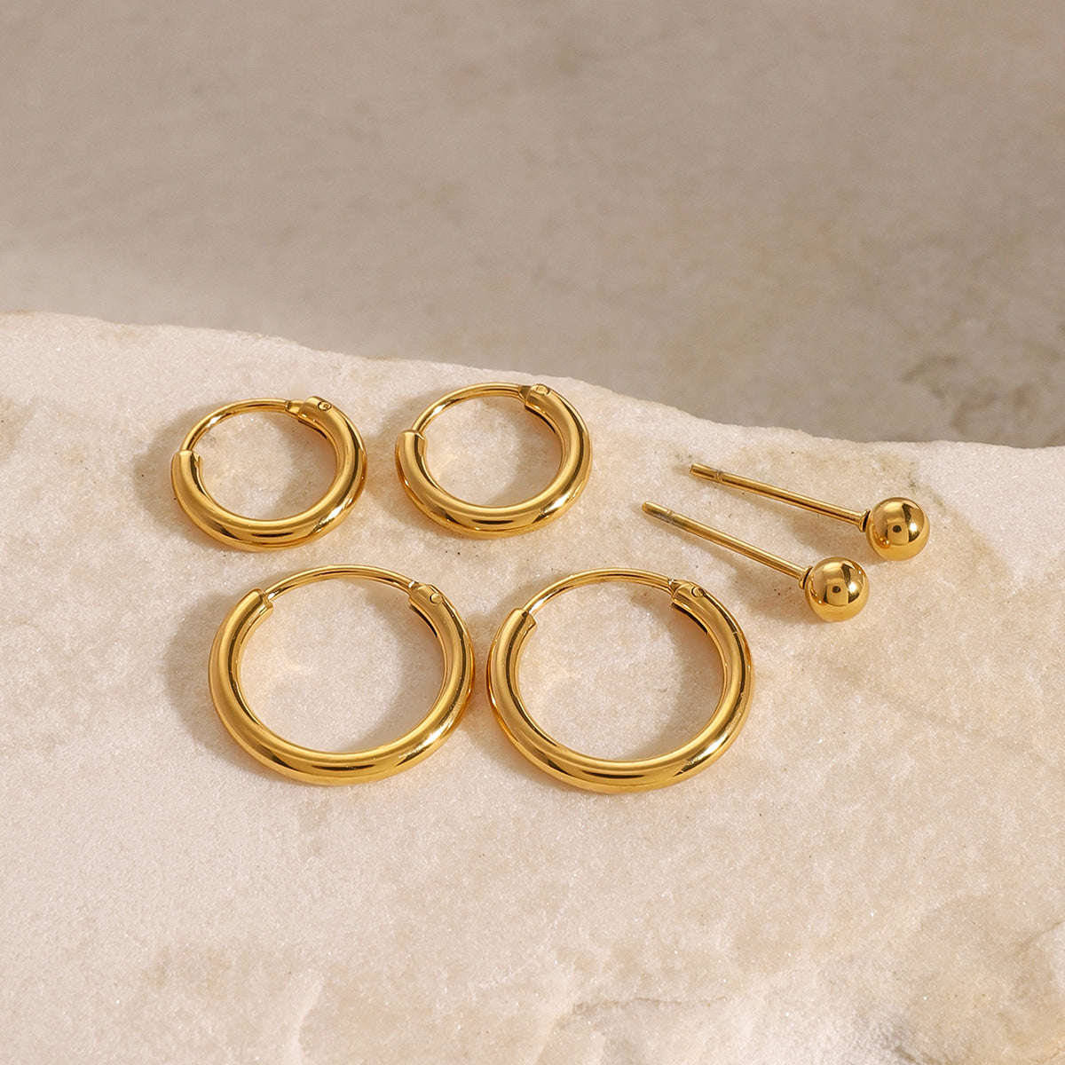 Classic gold hoop earrings and polished ball studs, clean product background for online store