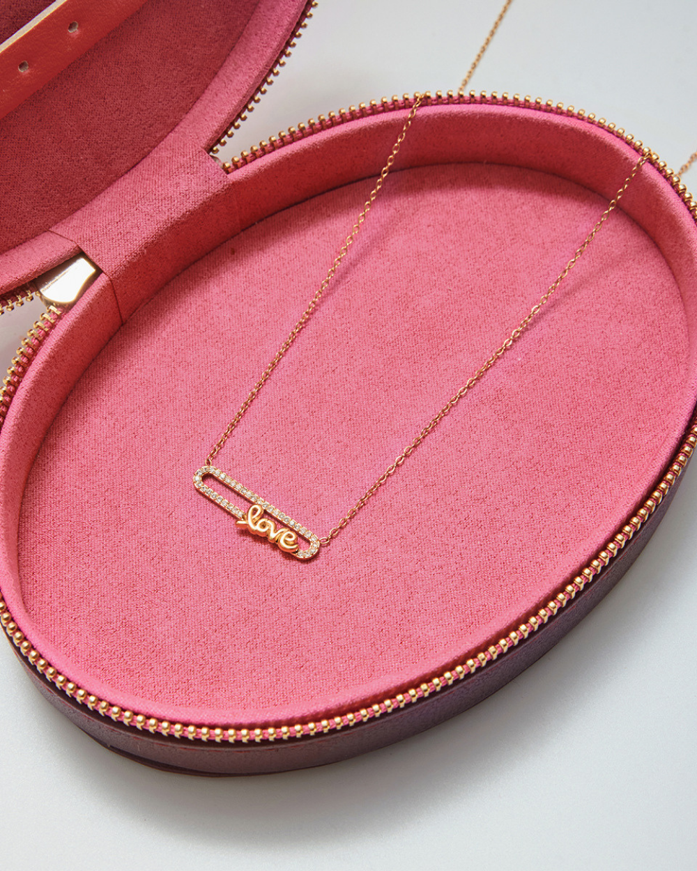 Gold LOVE necklace presented inside a pink jewelry case, emphasizing the dainty chain and detailed letter pendant.