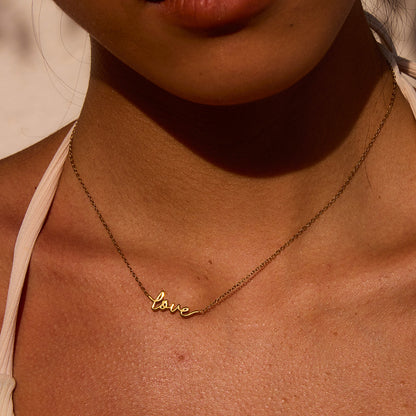 Golden hour close-up of "love" necklace worn with strappy white top