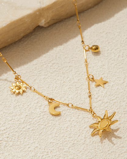 Gold necklace with sun and moon charms on a textured beige surface