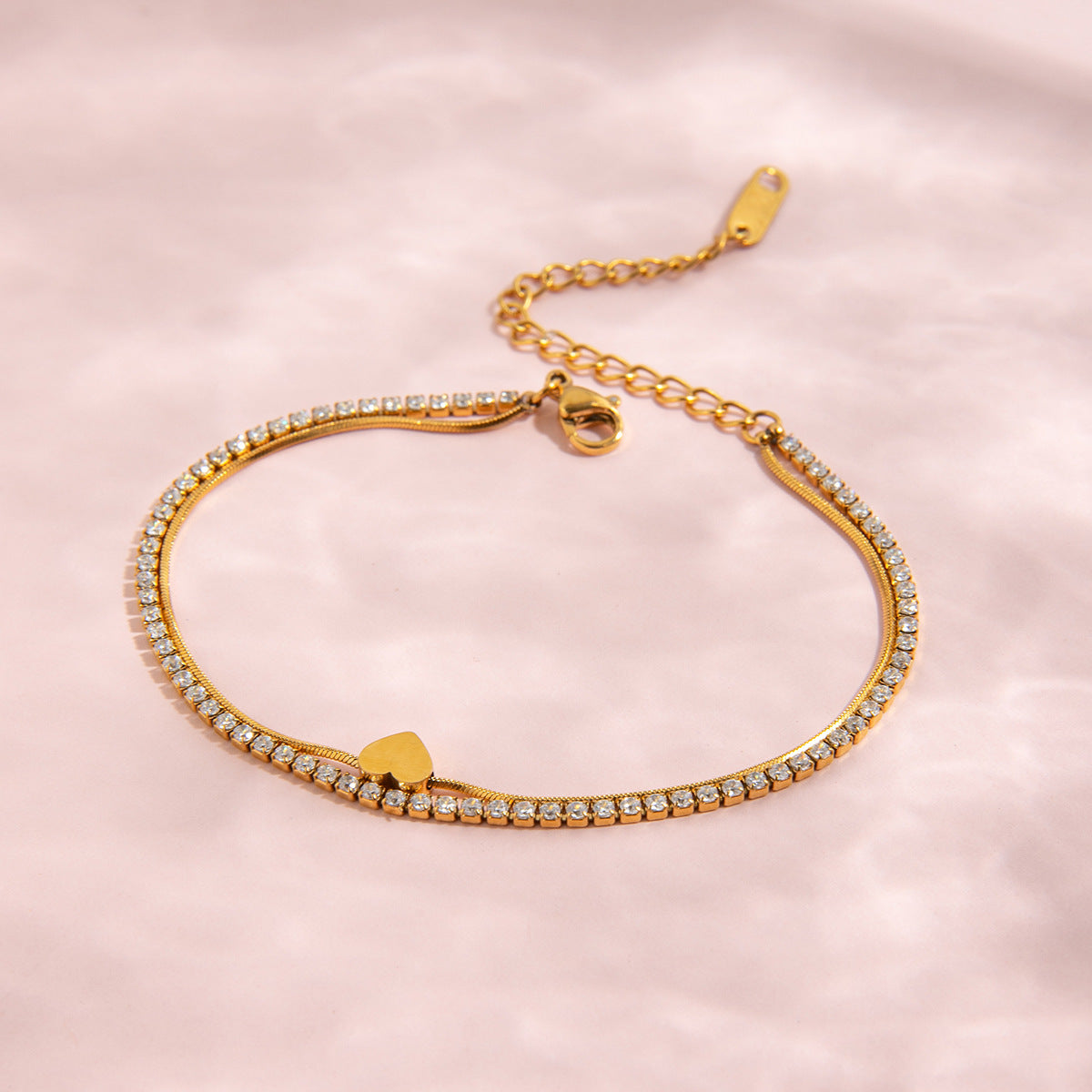 Gold bracelet with heart charm on a pink background