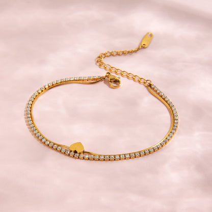 Gold bracelet with heart charm on a pink background