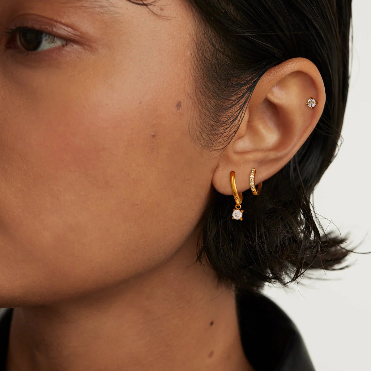 Model wearing layered gold hoops and crystal studs in a chic casual style, close-up on ear.