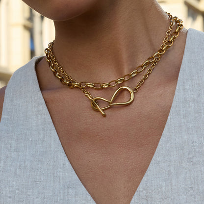 Gold chain necklace with a heart clasp worn by a person in a light blue top.