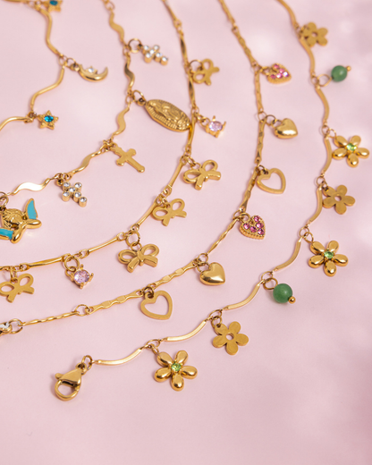 Gold necklaces with various charms on a pink background